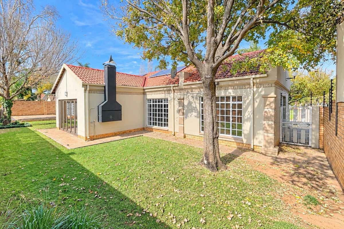Rear view of the townhouse featuring a private garden, paved patio area, external fireplace, and secure boundary walling.