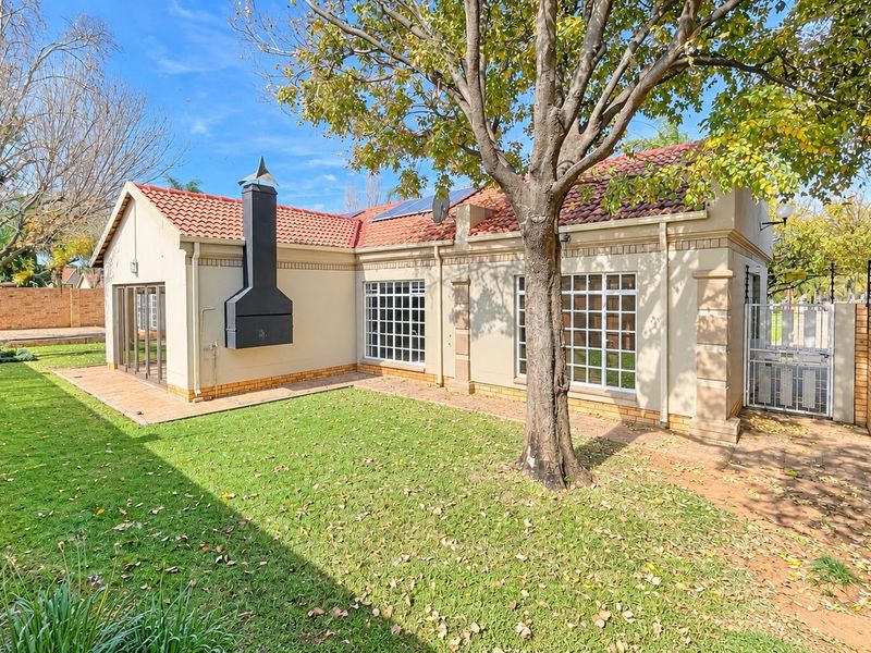Rear view of the townhouse featuring a private garden, paved patio area, external fireplace, and secure boundary walling.