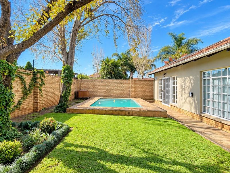 A private rear garden featuring a swimming pool with tiled surround, established lawn, and brick boundary walls, adjacent to the townhouse living area.