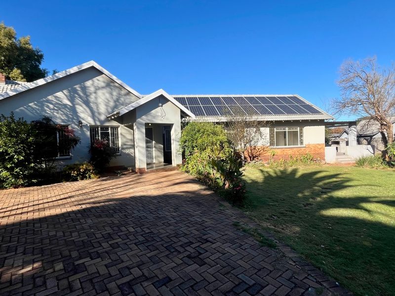 Front view of a single-story house featuring a brick paved driveway, well-maintained lawn, and a roof equipped with solar panels.