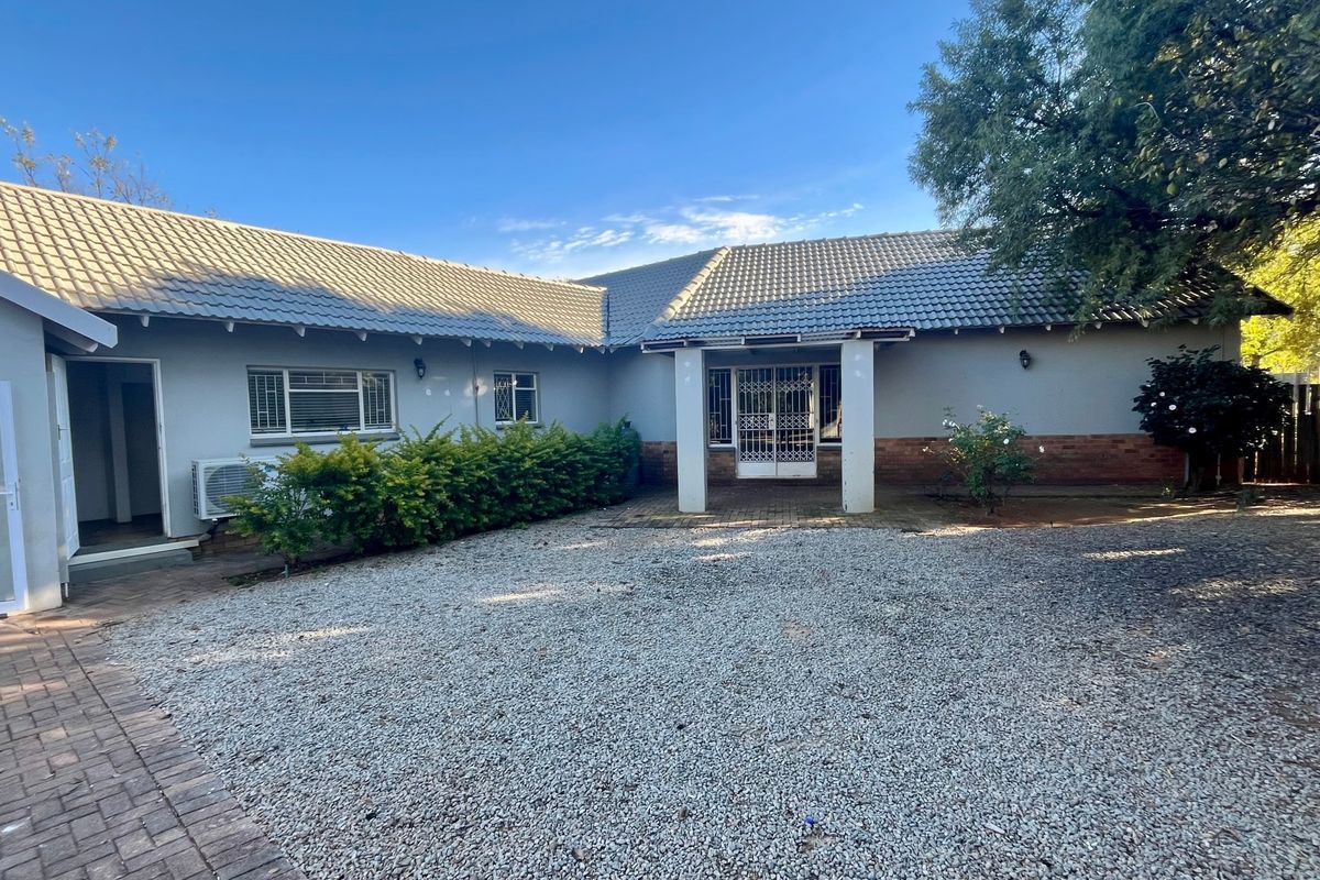 Rear view of the property featuring a tiled roof, brick and plaster facade, security gate, and a combination of paved and gravel outdoor areas.