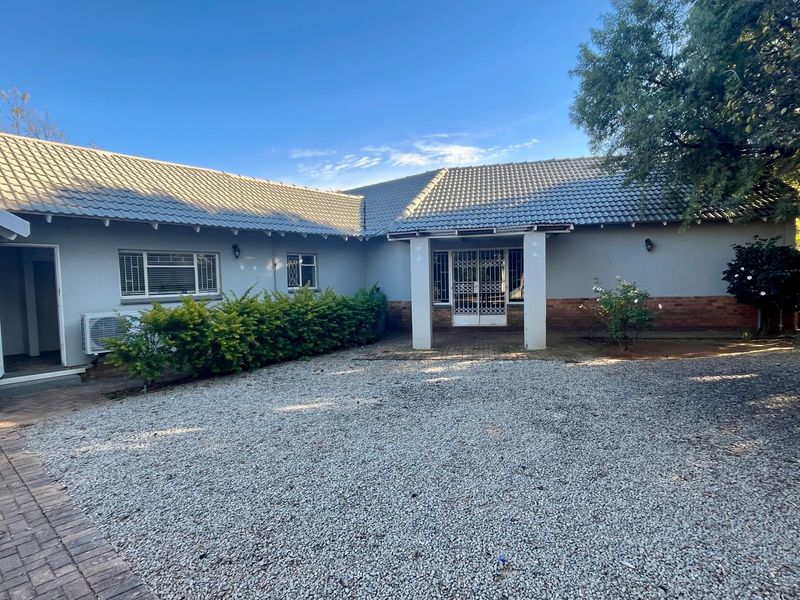Rear view of the property featuring a tiled roof, brick and plaster facade, security gate, and a combination of paved and gravel outdoor areas.