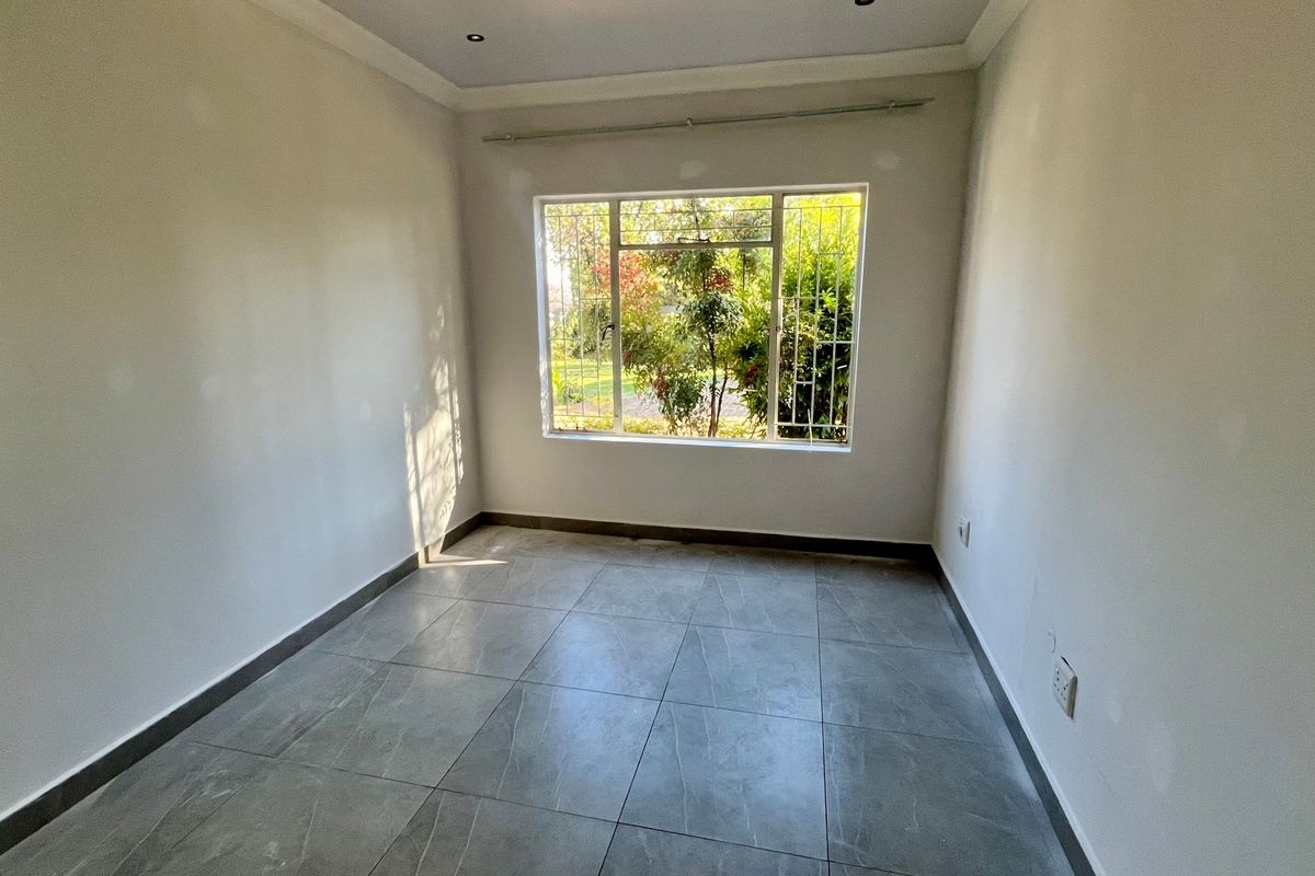 A bright, empty bedroom featuring modern grey tiled flooring, recessed downlights, and a large window with security bars.