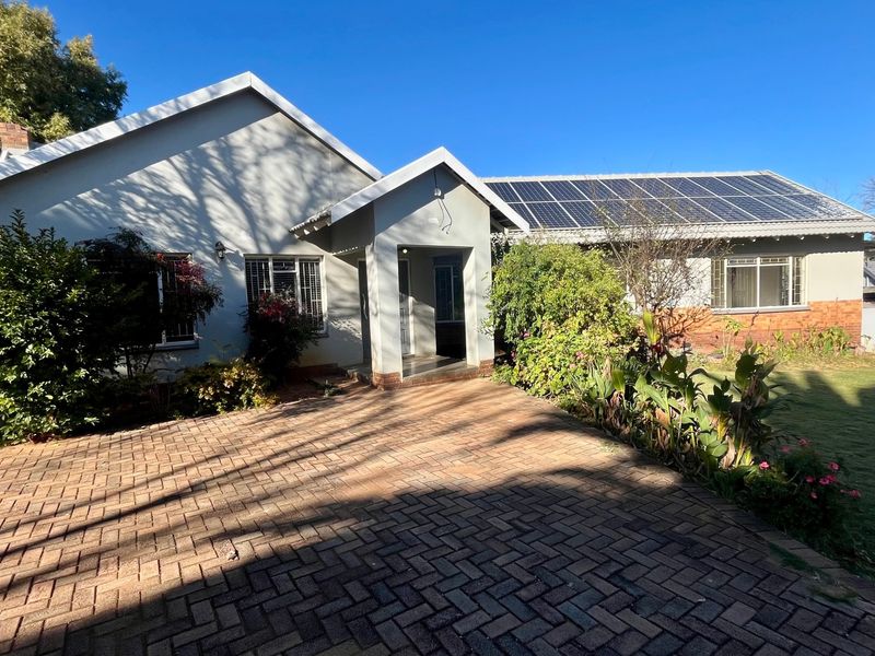 Front view of a single-story house featuring a paved driveway, covered entrance, and roof-mounted solar panels set within a landscaped garden.