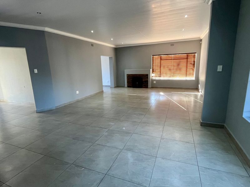 Spacious, open-plan living area featuring neutral grey walls, large format floor tiles, recessed lighting, and a central fireplace.