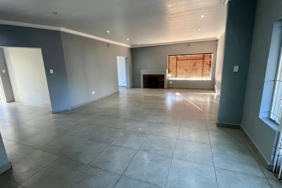 Spacious, open-plan living area featuring neutral grey walls, large format floor tiles, recessed lighting, and a central fireplace.