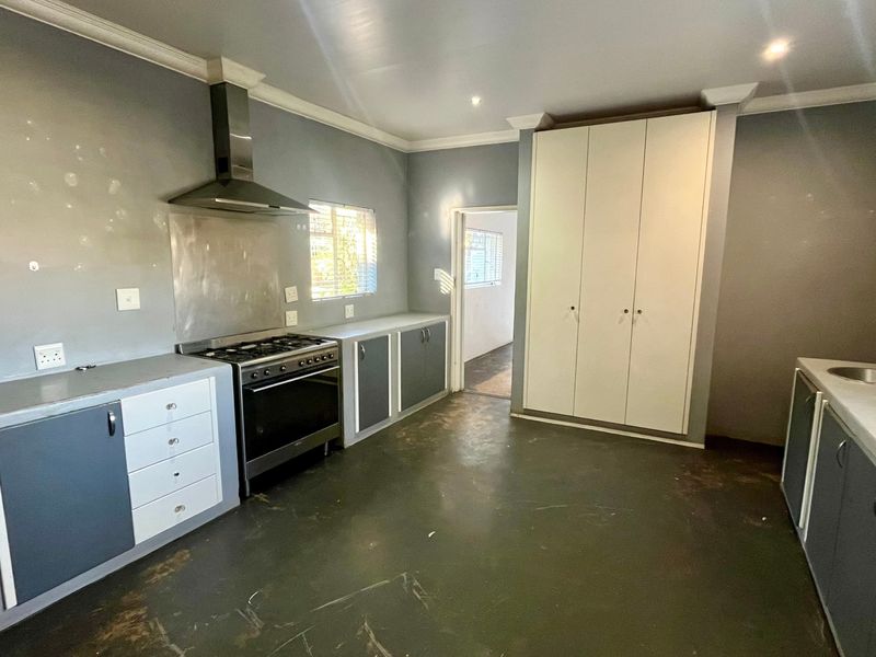 A spacious kitchen featuring built-in cabinetry, a stainless steel extractor fan, a gas stove, and a large pantry cupboard, requiring cosmetic updates.