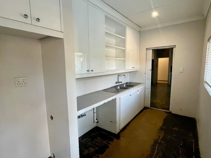 A functional laundry room featuring built-in white cabinetry, a stainless steel sink, and plumbing connections, currently requiring floor and wall finish repairs.