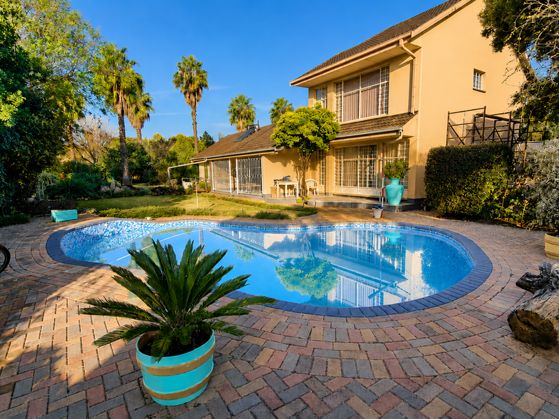 A well-maintained rear garden featuring a swimming pool surrounded by brick paving and mature landscaping, adjacent to the main house structure.