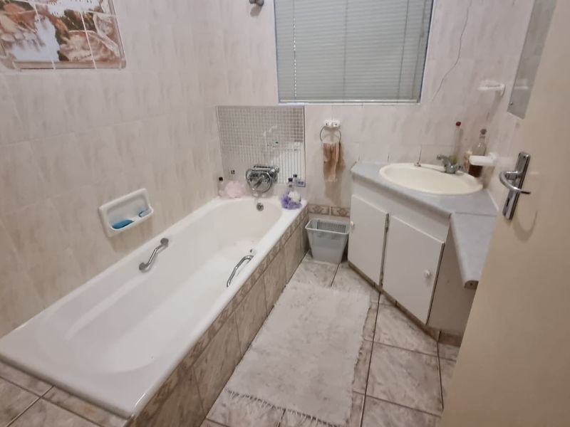 A functional bathroom featuring a built-in bathtub, vanity cabinet with basin, and tiled finishes throughout.