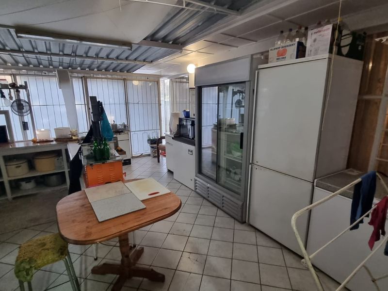 A functional scullery or utility area featuring tiled flooring, built-in shelving, and exposed ceiling structure, providing ample space for food preparation and storage.