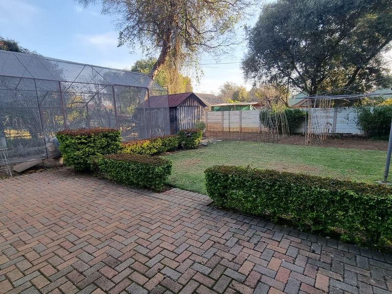 Rear garden featuring brick paved patio, lawn area, established hedges, and a large wire mesh enclosure structure.