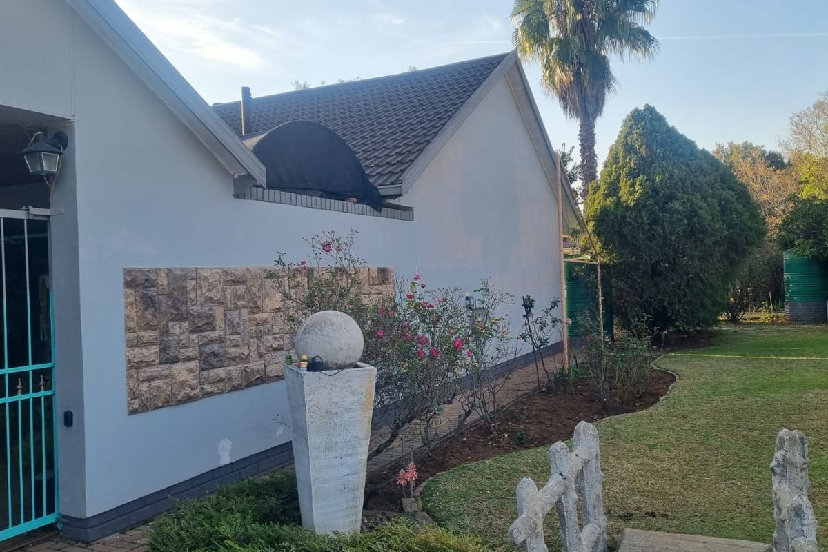 Rear exterior view of the house featuring a tiled roof, stone cladding accent wall, security gate, and a well-maintained garden area.
