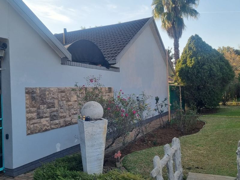 Rear exterior view of the house featuring a tiled roof, stone cladding accent wall, security gate, and a well-maintained garden area.
