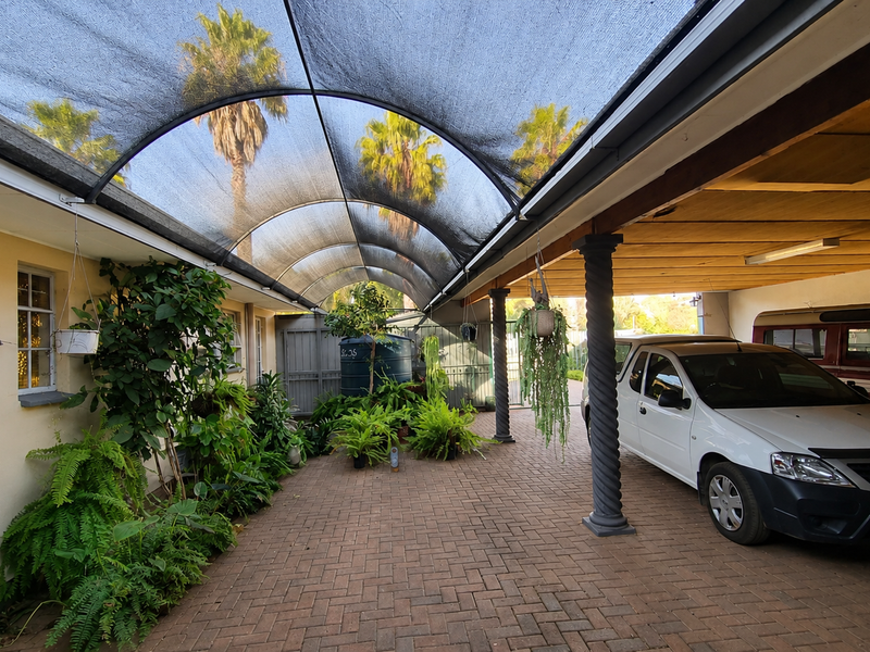 A covered outdoor parking area featuring a curved shade cloth canopy, paved flooring, and decorative columns, providing a functional space for vehicles.