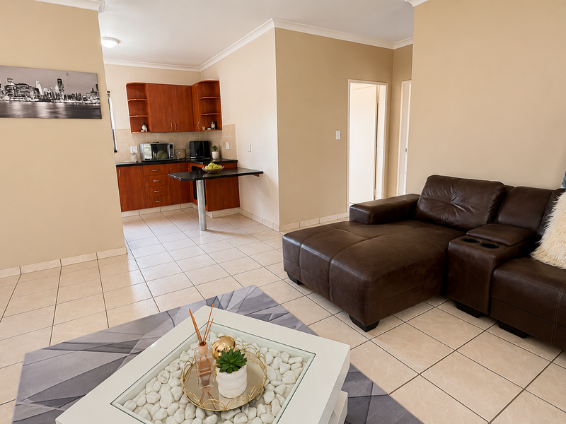 An open-plan living and kitchen area featuring tiled flooring, neutral wall tones, and a functional kitchen layout with built-in cabinetry and a breakfast bar.