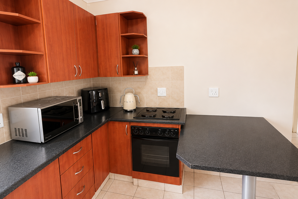 Compact kitchen featuring wood-finish cabinetry, dark laminate countertops, built-in oven and hob, tiled backsplash, and an integrated breakfast bar.