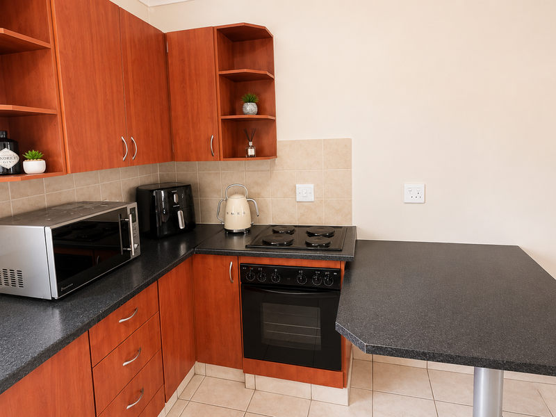 Compact kitchen featuring wood-finish cabinetry, dark laminate countertops, built-in oven and hob, tiled backsplash, and an integrated breakfast bar.