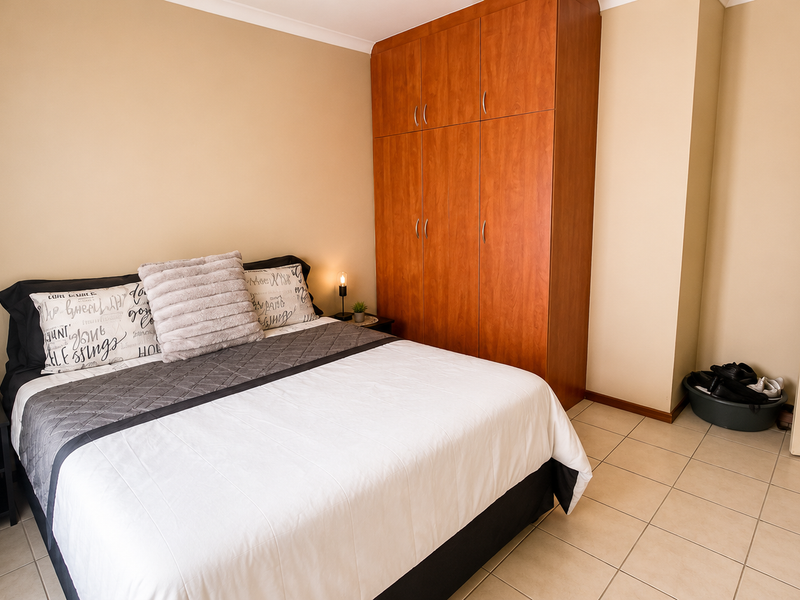A bedroom featuring tiled flooring and a large built-in wooden wardrobe, providing ample storage space.