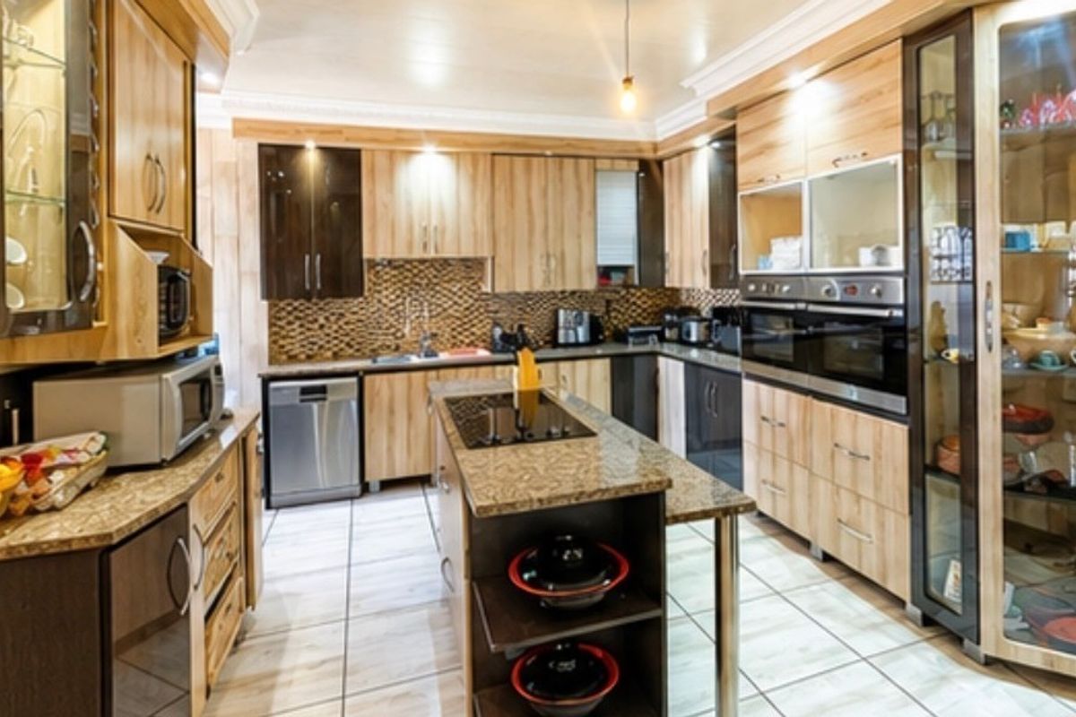 A well-appointed kitchen featuring extensive wooden cabinetry, granite countertops, a central island with a hob, and integrated double ovens with modern finishes.