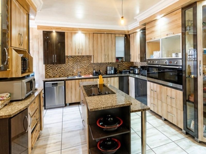 A well-appointed kitchen featuring extensive wooden cabinetry, granite countertops, a central island with a hob, and integrated double ovens with modern finishes.