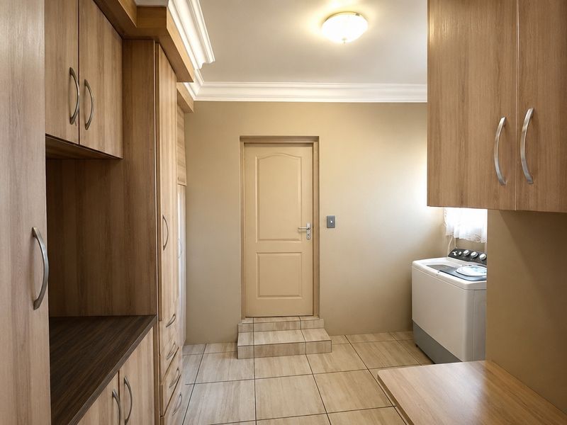 A functional laundry room featuring ample built-in wooden cabinetry, tiled flooring, and a raised doorway leading to an adjacent area.