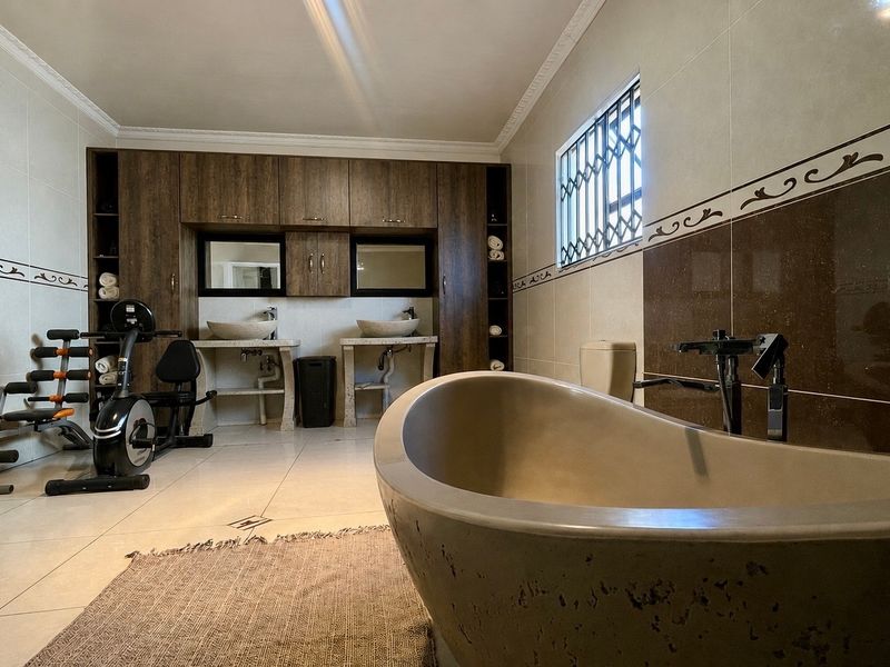 Spacious bathroom featuring a modern freestanding bathtub, double vanity with vessel sinks, built-in cabinetry, and neutral wall and floor tiling.
