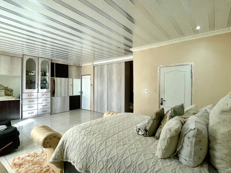 Spacious bedroom featuring extensive built-in cabinetry, tiled flooring, and a unique panelled ceiling design with recessed lighting.