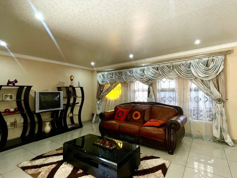 A spacious living room featuring neutral walls, polished porcelain floor tiles, recessed downlighting, and decorative ceiling cornicing.