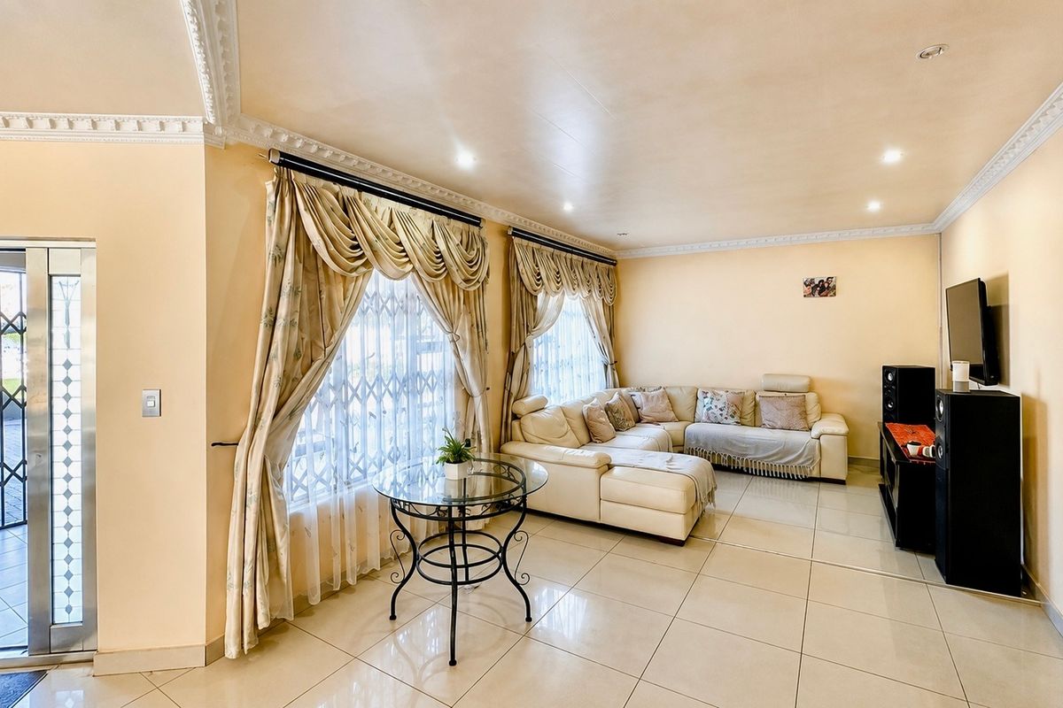 A spacious living room featuring large windows with security gates, tiled flooring, and decorative crown molding, providing a comfortable and functional living space.