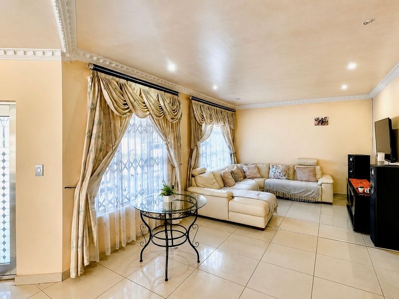 A spacious living room featuring large windows with security gates, tiled flooring, and decorative crown molding, providing a comfortable and functional living space.