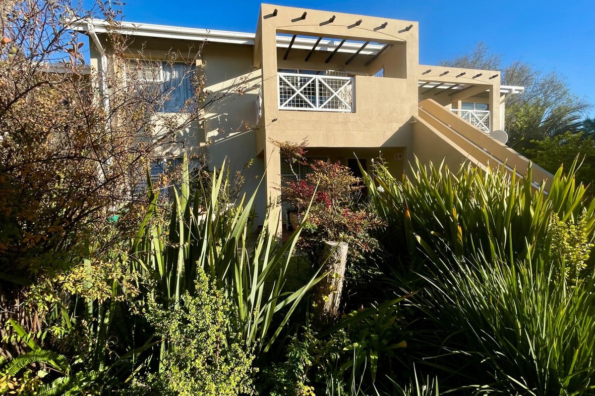Rear view of the apartment building featuring a balcony with a pergola and an external staircase, surrounded by established garden landscaping.