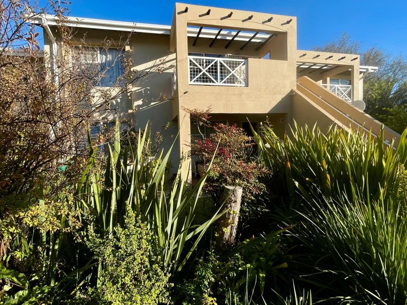 Rear view of the apartment building featuring a balcony with a pergola and an external staircase, surrounded by established garden landscaping.