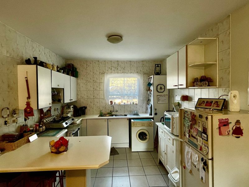 A functional kitchen featuring tiled walls and flooring, built-in cabinetry, a double basin sink, and a breakfast counter, offering potential for modern renovation.