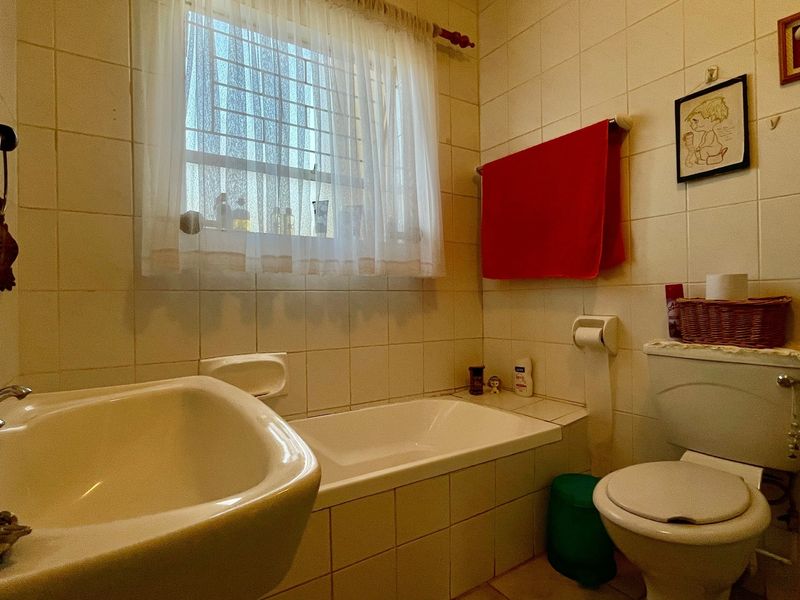 A functional bathroom featuring a bathtub, toilet, and washbasin with neutral wall tiling and a window with security bars.