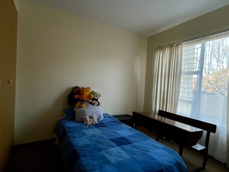 A functional bedroom featuring a built-in wardrobe and a large window with security bars, providing natural light and storage space.