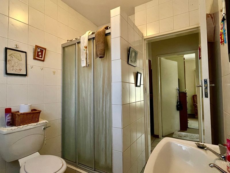 A functional bathroom featuring a shower enclosure, toilet, and washbasin with full-height wall tiling.