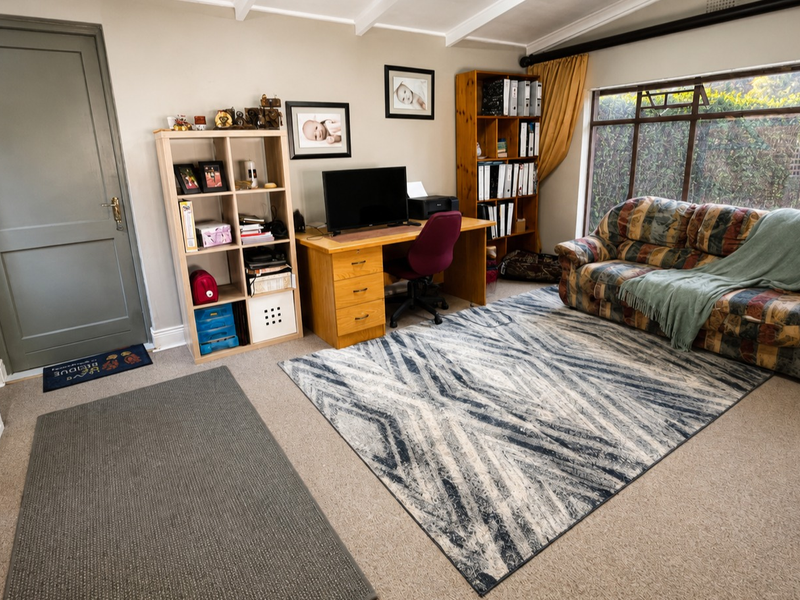 A multi-purpose living area featuring exposed ceiling beams, a large window overlooking the garden, and neutral wall finishes.