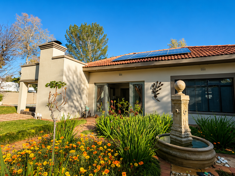 Rear view of the house featuring a landscaped garden, stone fountain, paved patio area, and roof-mounted solar panels.