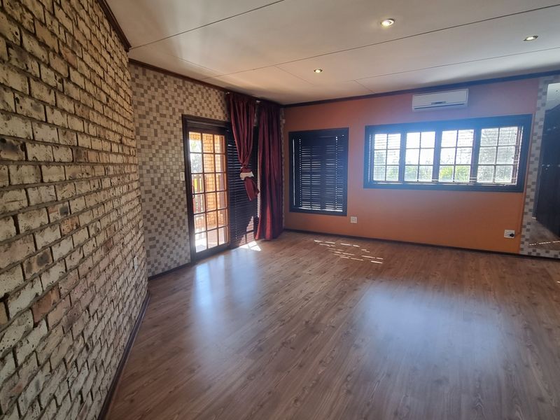 Spacious bedroom featuring laminate flooring, an exposed brick feature wall, split-system air conditioning, and direct access to an outdoor area via a sliding door.