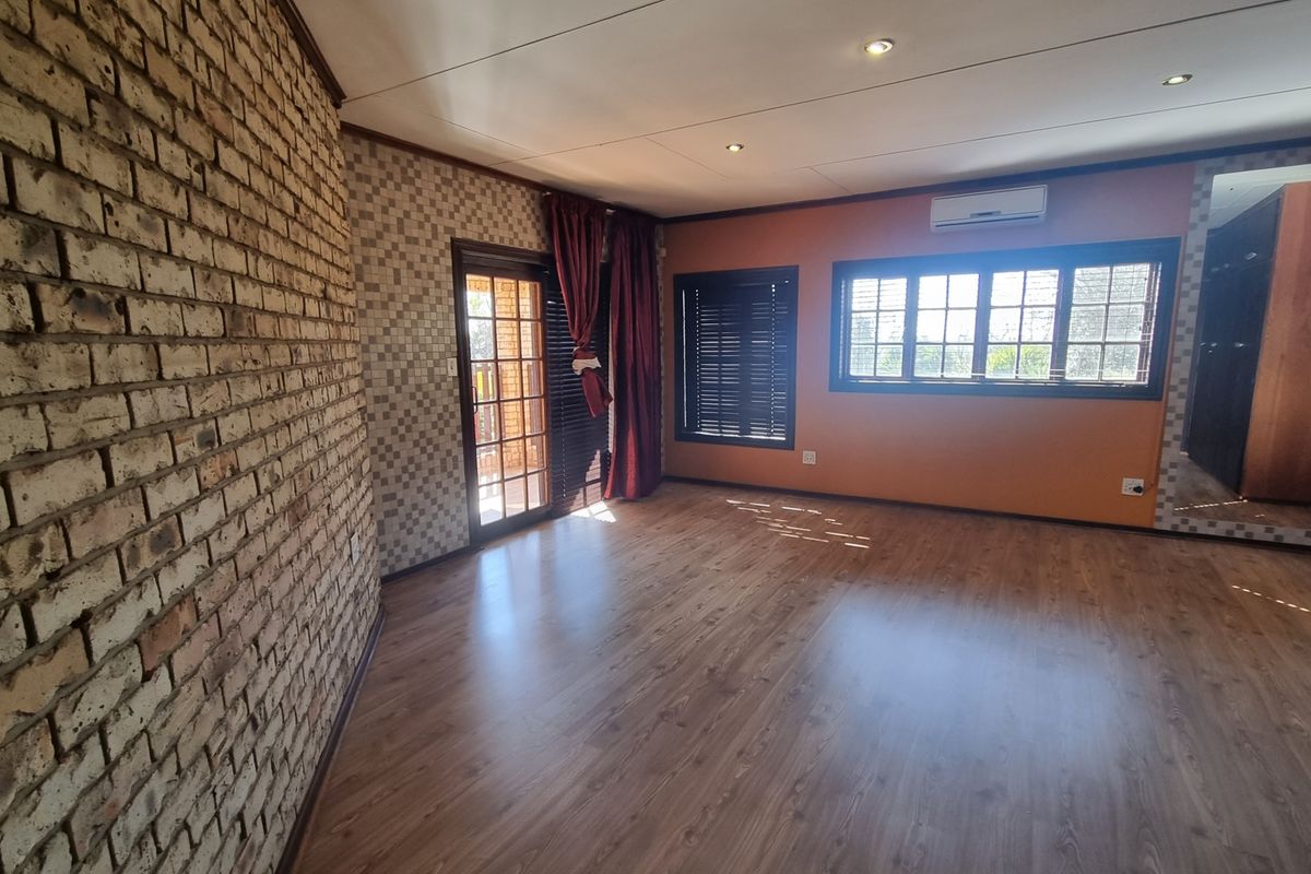 Spacious bedroom featuring laminate flooring, an exposed brick feature wall, split-system air conditioning, and direct access to an outdoor area via a sliding door.