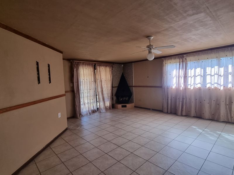Spacious living room featuring tiled flooring, a corner fireplace, and a ceiling fan, offering a blank canvas for renovation and interior design updates.