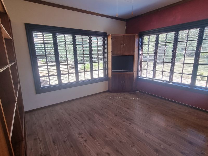 An empty living room featuring laminate flooring, built-in corner cabinetry, and large windows with venetian blinds.
