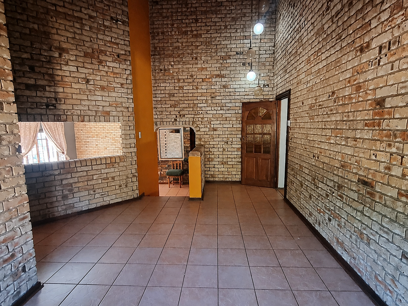 Spacious living area featuring distinctive exposed brick walls, ceramic tile flooring, and a classic timber door, offering a rustic architectural aesthetic.