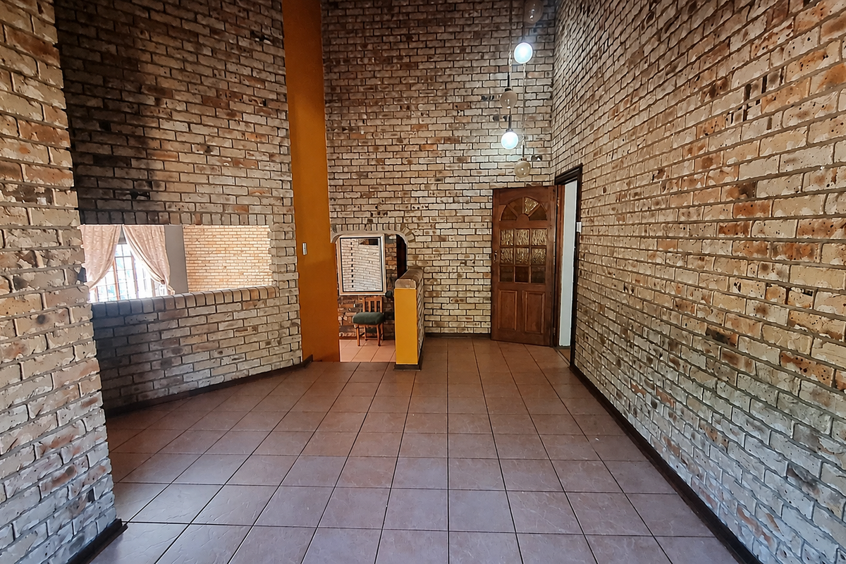 Spacious living area featuring distinctive exposed brick walls, ceramic tile flooring, and a classic timber door, offering a rustic architectural aesthetic.