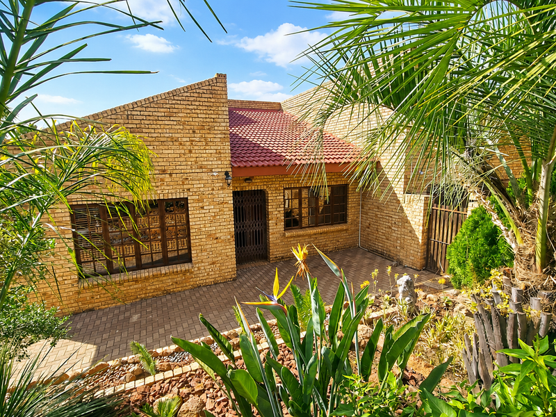 A well-maintained face brick house featuring a tiled roof, paved entrance area, and secure metal window frames, surrounded by established garden landscaping.