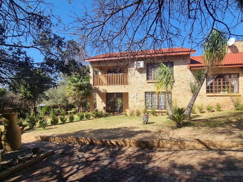 Rear view of a double-story face brick house featuring a tiled roof, timber balcony, and a paved driveway set within a landscaped garden.