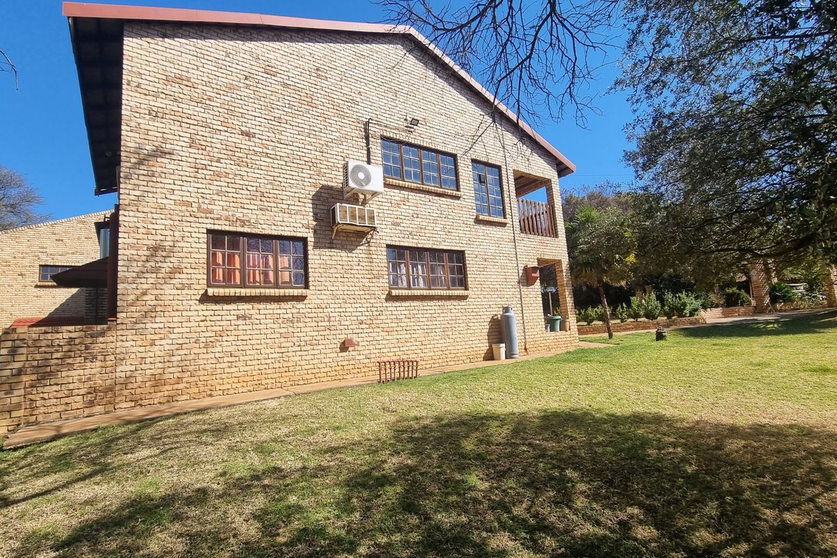 Rear view of a face brick house featuring timber-framed windows, an external air conditioning unit, and a small balcony overlooking the garden.