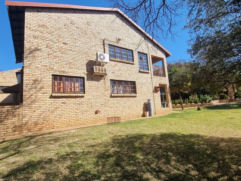 Rear view of a face brick house featuring timber-framed windows, an external air conditioning unit, and a small balcony overlooking the garden.