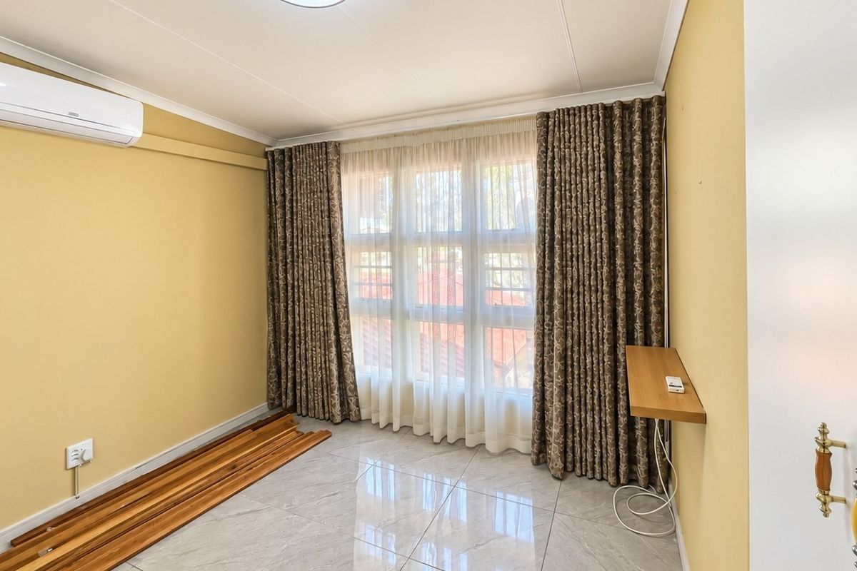 A bright, empty bedroom featuring polished tiled flooring, a wall-mounted air conditioning unit, and large windows with floor-to-ceiling curtains.